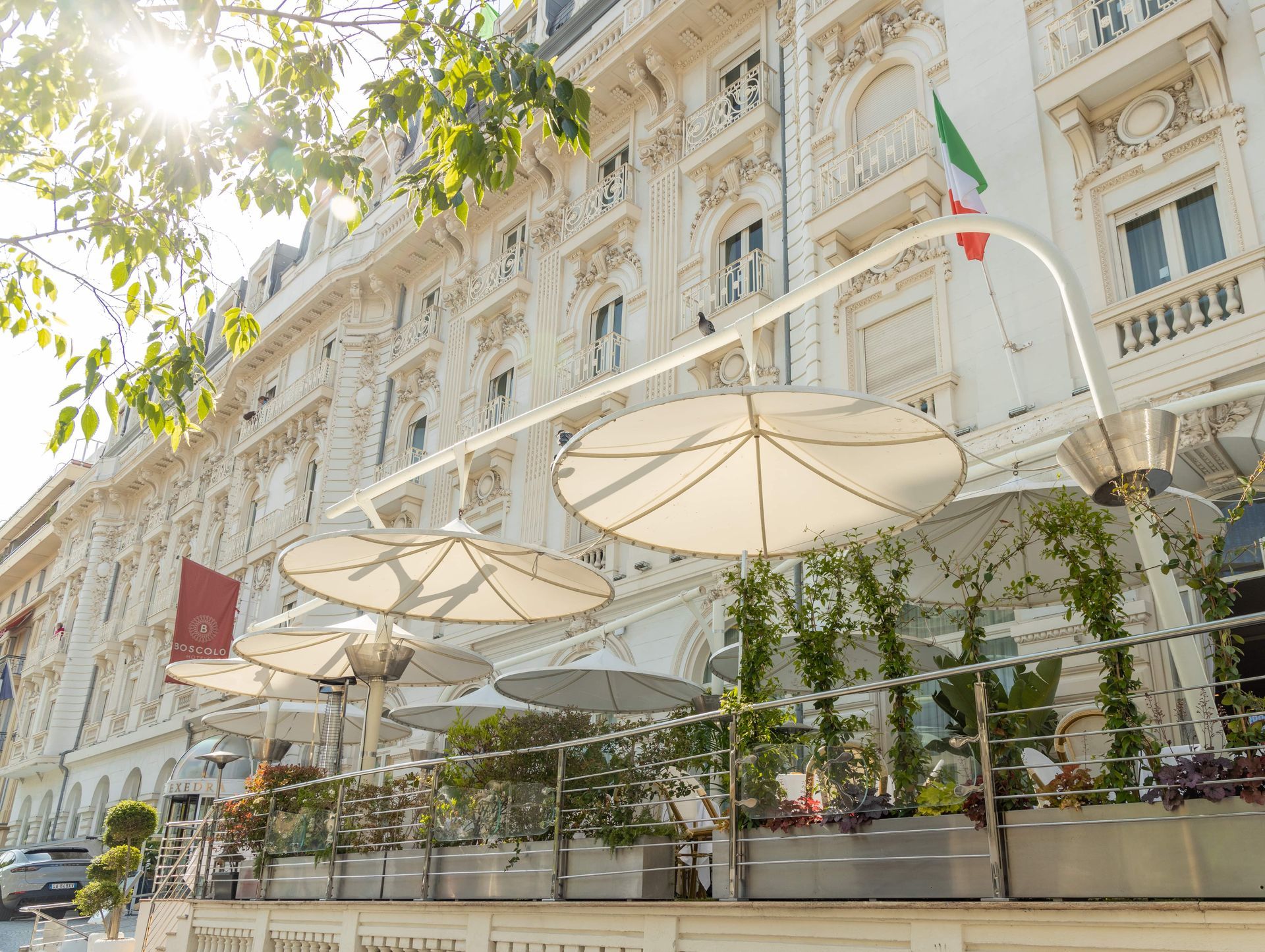 Elegant white café terrace with large umbrellas and potted plants beside an ornate building façade