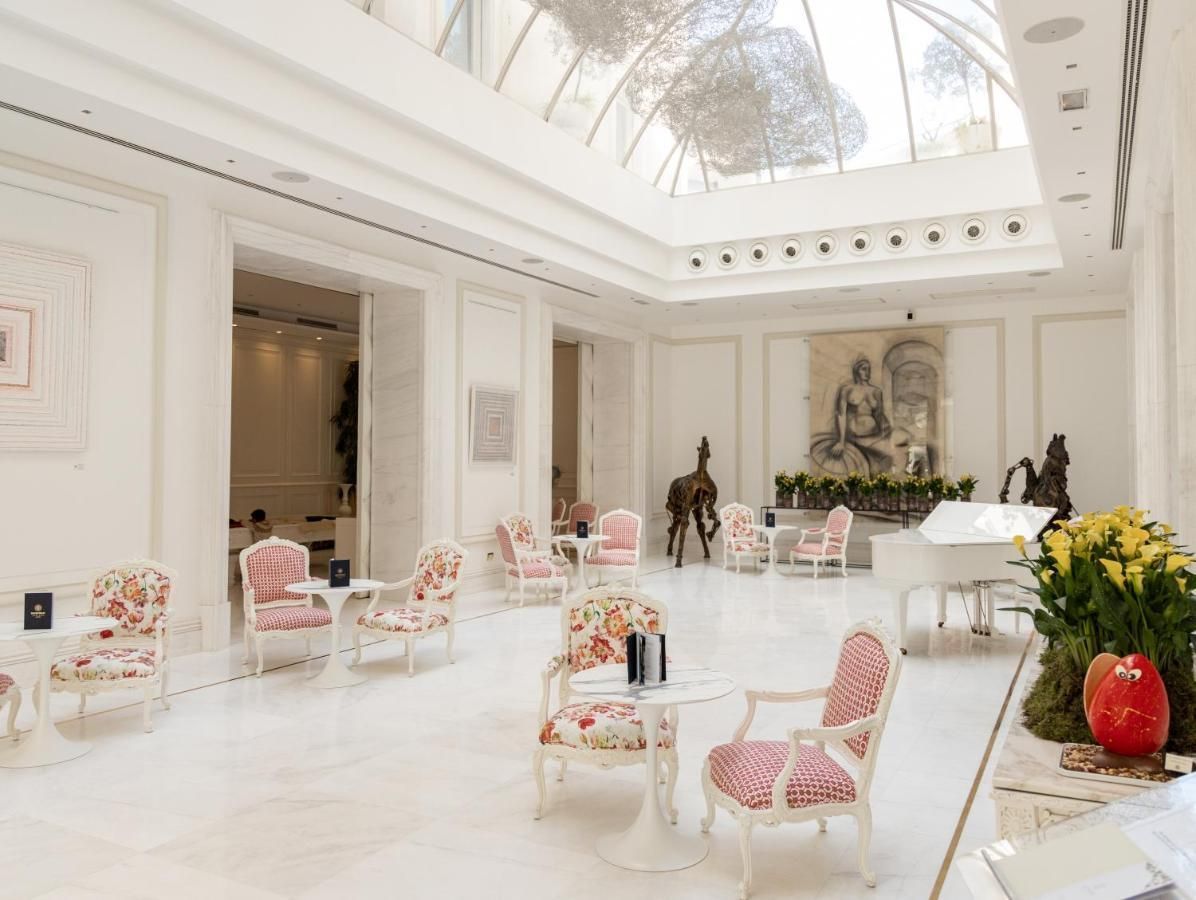 Bright white luxury lounge with pink chairs, marble floors, and floral arrangements beneath a skylight