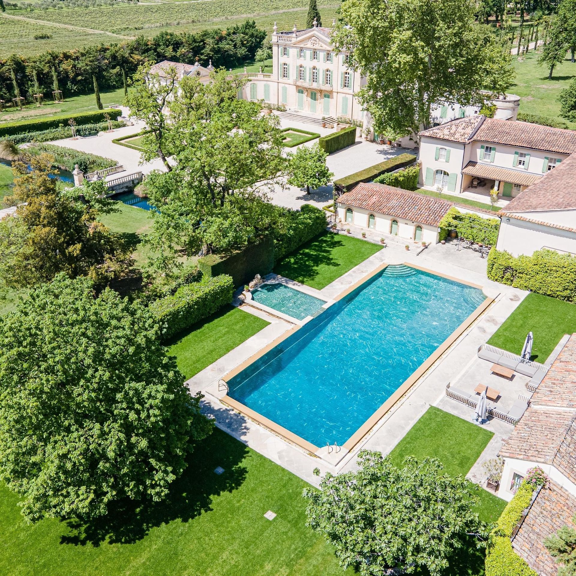 Aerial view of a villa estate with a large blue swimming pool, gardens, and surrounding buildings