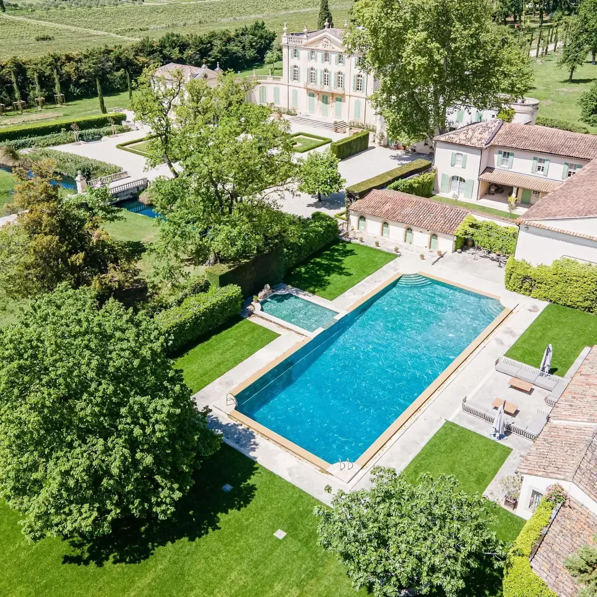 Aerial view of a villa estate with a large blue swimming pool, gardens, and surrounding buildings