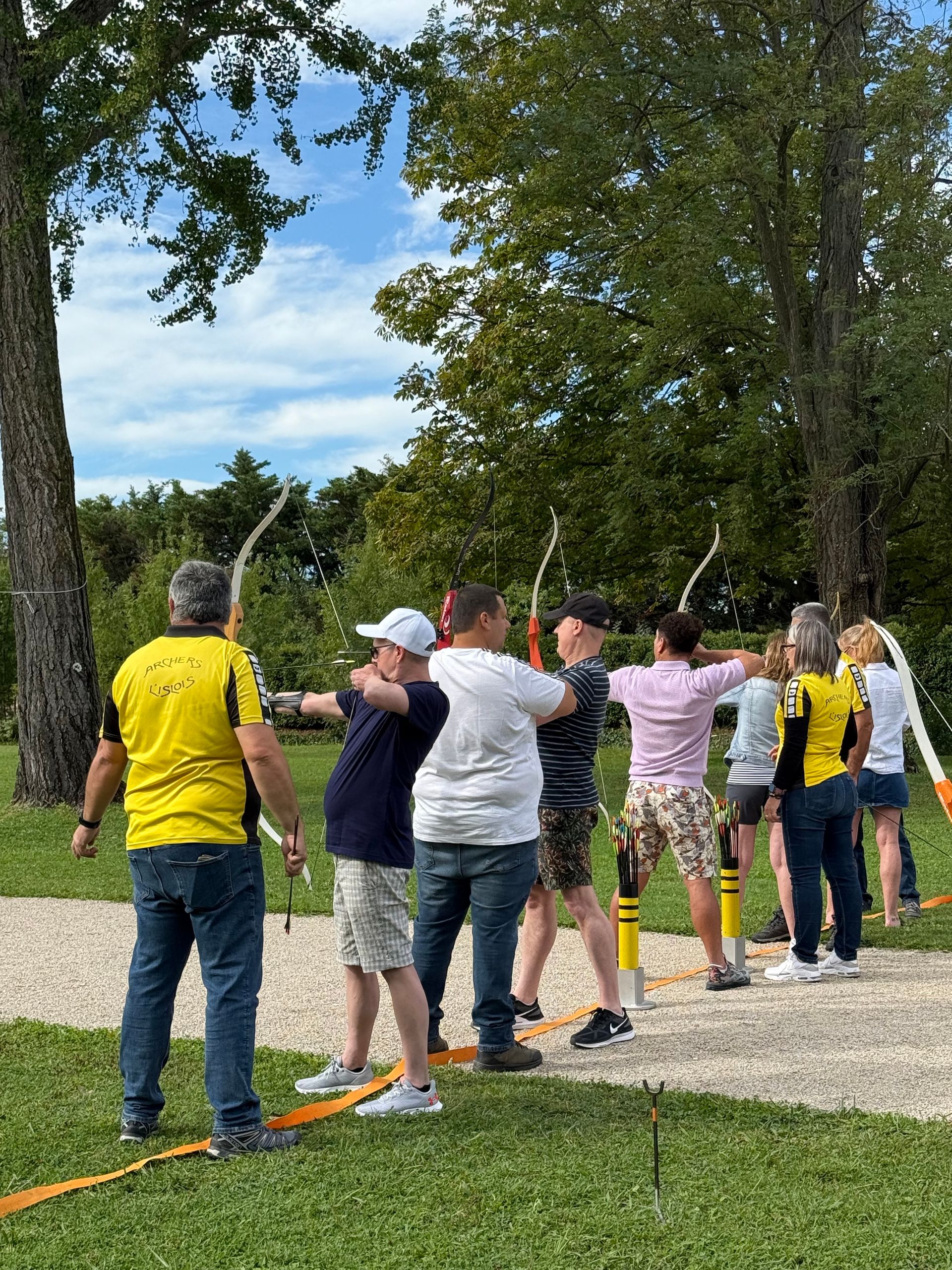People standing in a line outdoors, holding a rope in a park on a sunny day.