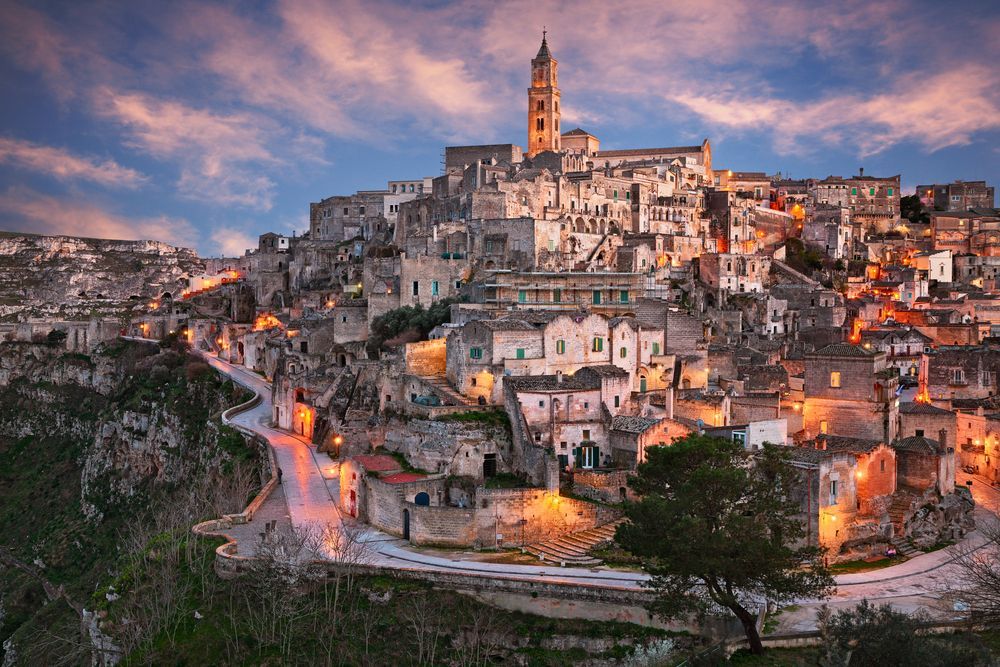 Hilltop village at dusk with stone buildings glowing under a pink-blue sky