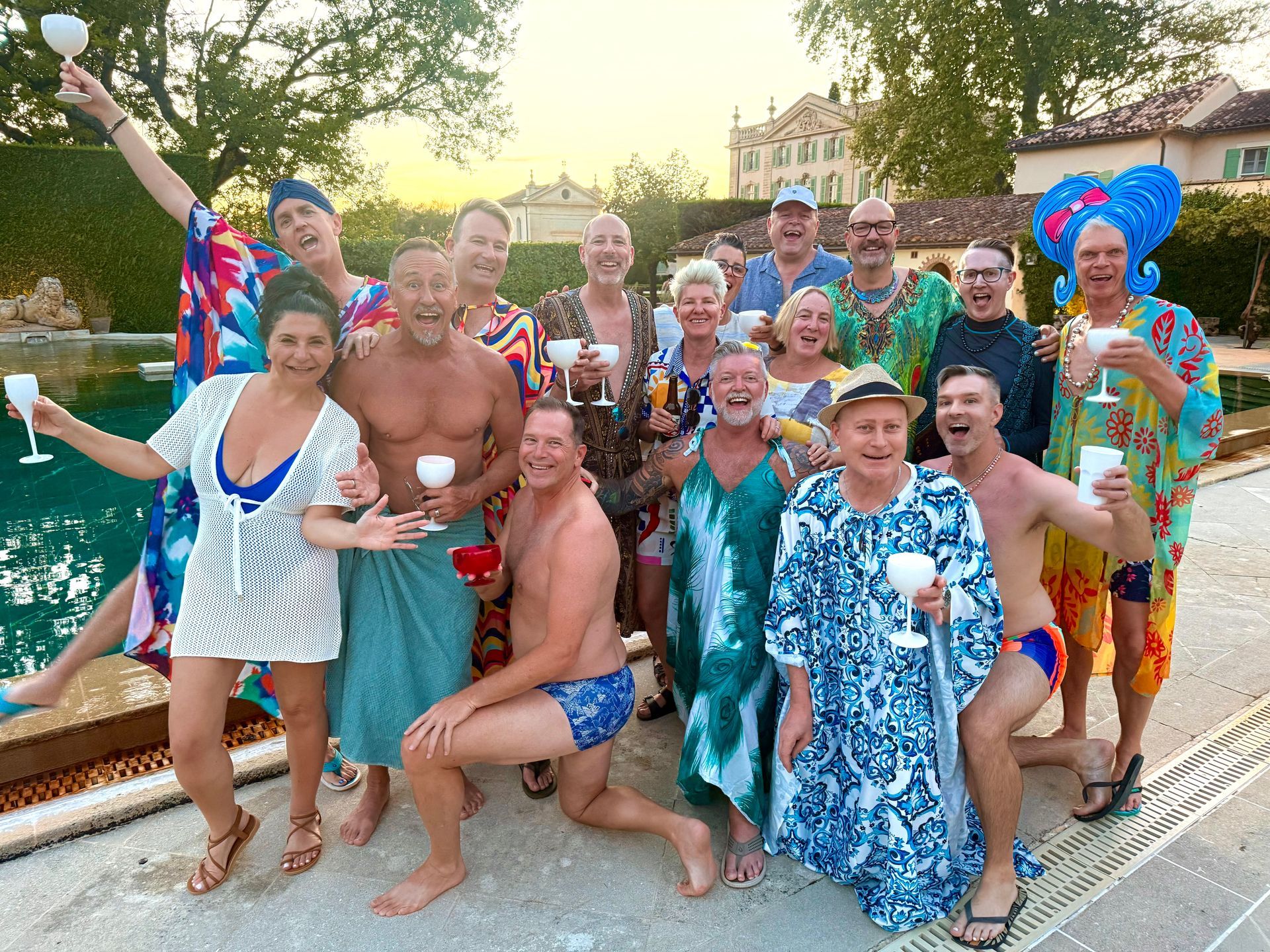 Group of people in colorful costumes posing and smiling by a pool during a festive outdoor gathering