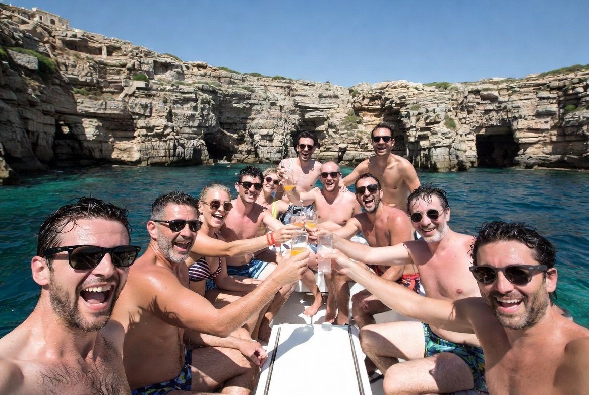 Group of friends smiling on a boat in a turquoise sea near rocky cliffs