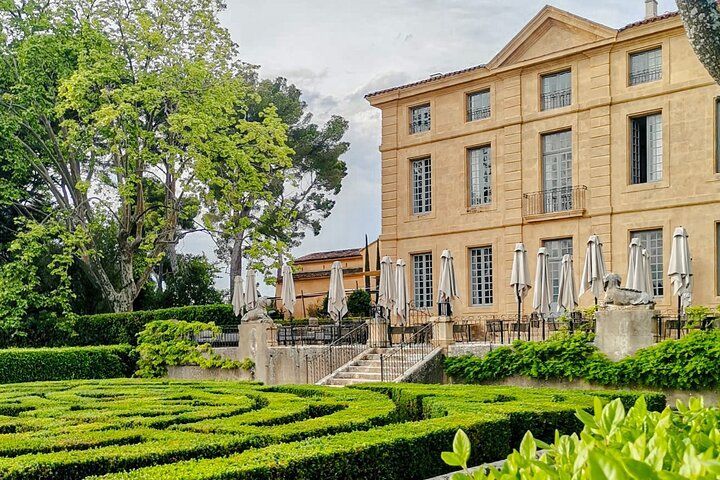 Manicured garden with hedges in front of a beige stone mansion with columns and patio umbrellas