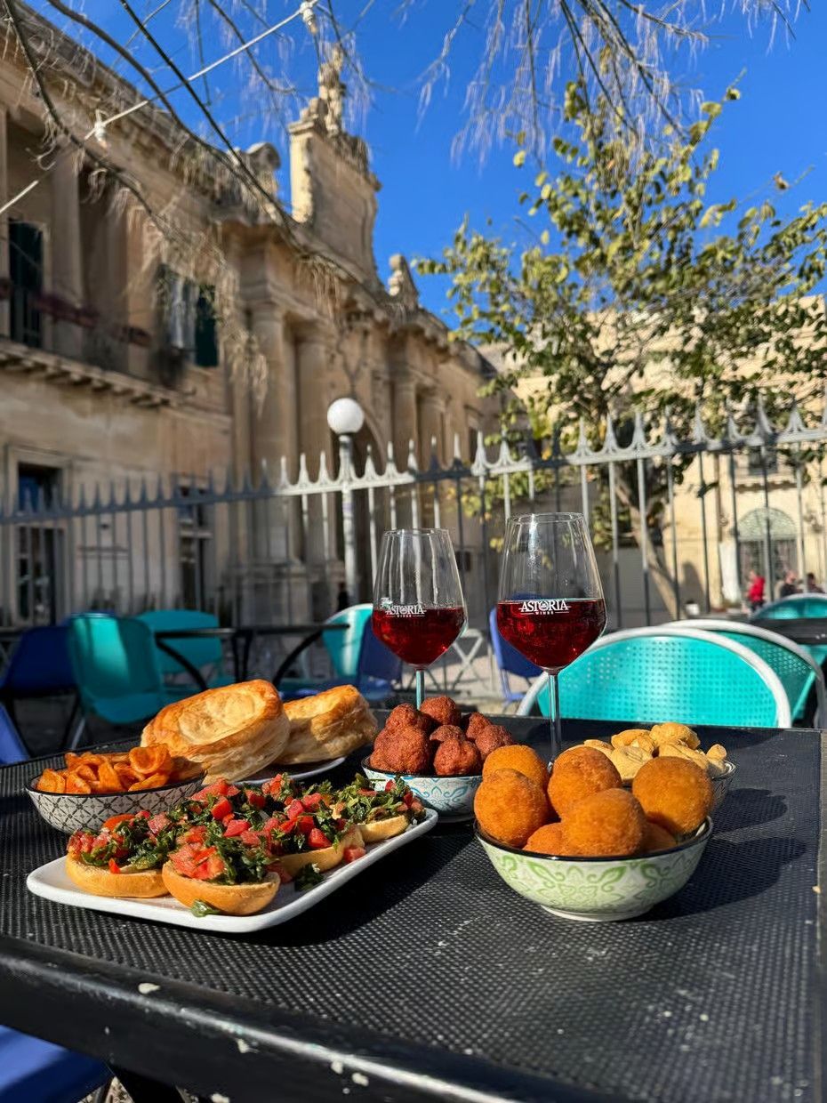 Outdoor table with salads, fried snacks, bread, and two glasses of red wine in a sunny courtyard