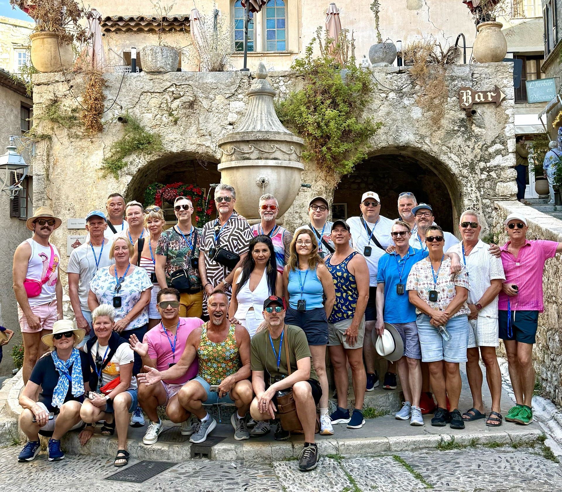 Group of tourists posing in front of a stone building with arches and a fountain.