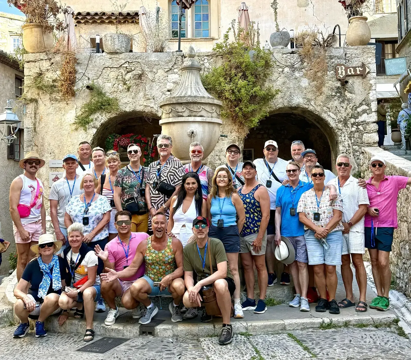Large group posing for a photo in front of a stone building with arches and a central fountain.