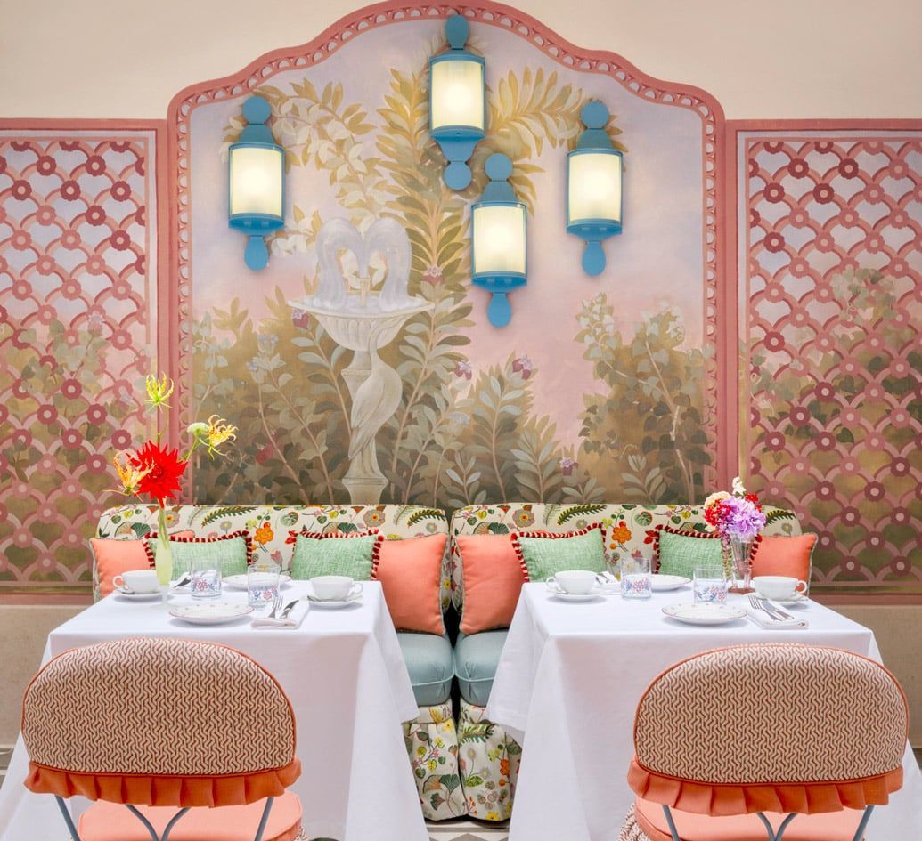 Elegant outdoor dining nook with pink walls, blue lanterns, and white tables set for two with flowers