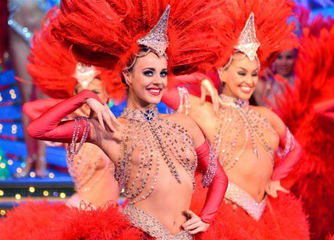 Dancers in red feather costumes and headpieces performing on a brightly lit stage