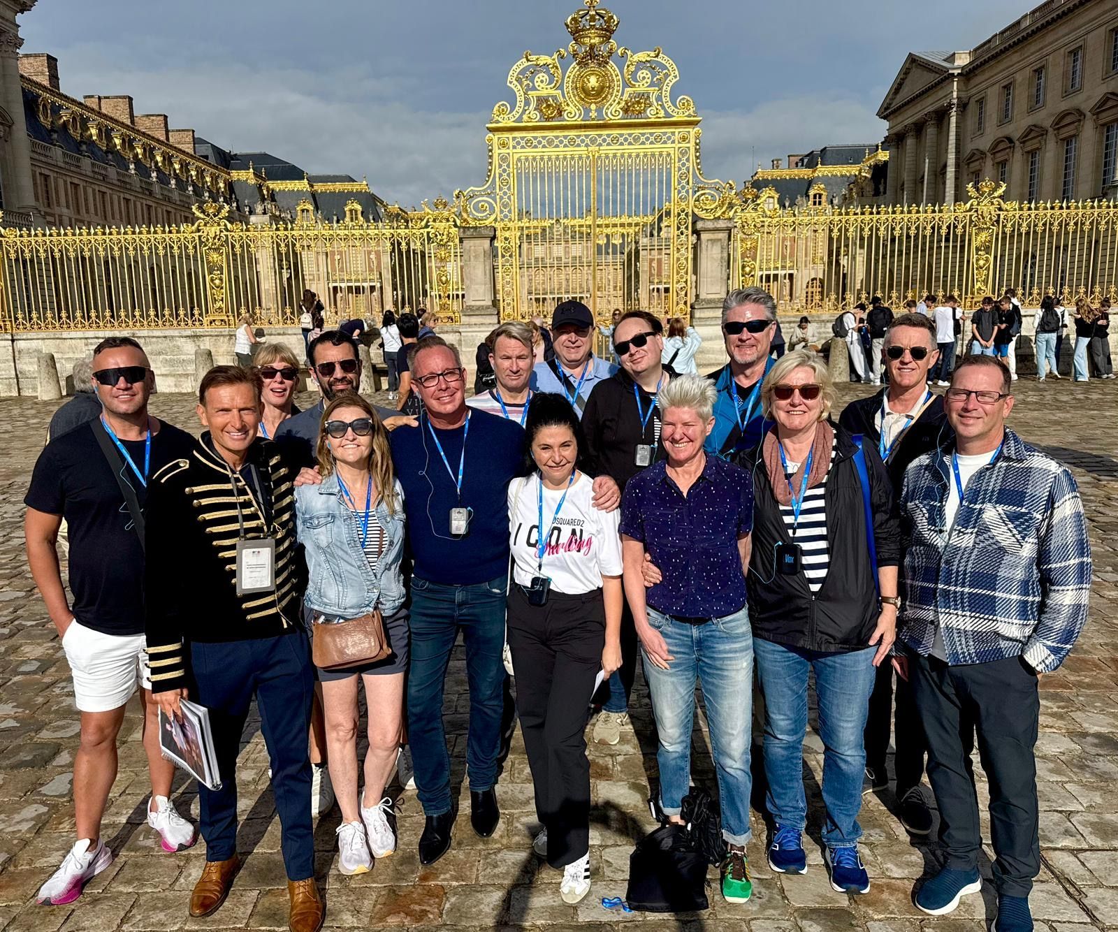 Group of people posing in front of a gold palace gate in a sunny outdoor courtyard.