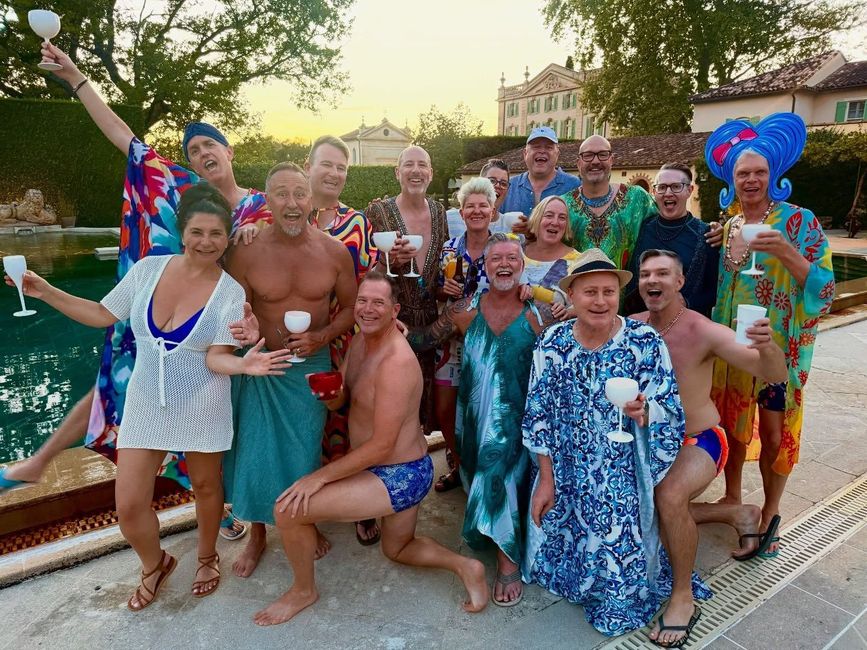 Group in colorful swimwear posing and smiling by a pool at sunset