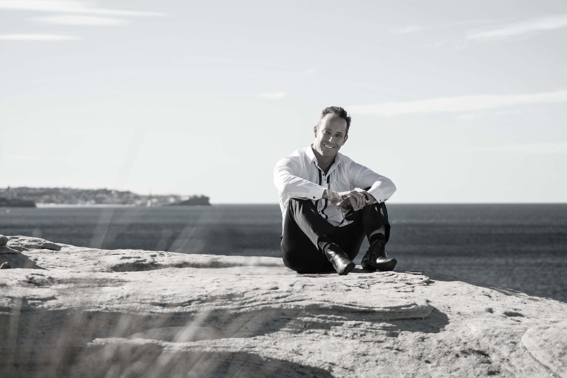 Person sitting on a rocky cliff overlooking the ocean under a bright sky