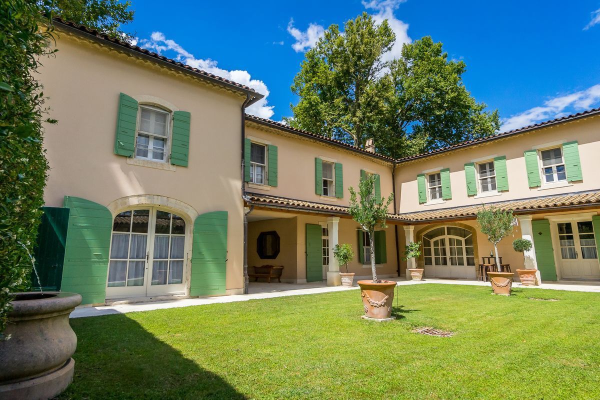 Sunlit Mediterranean-style courtyard with green shutters, arched windows, and a manicured lawn