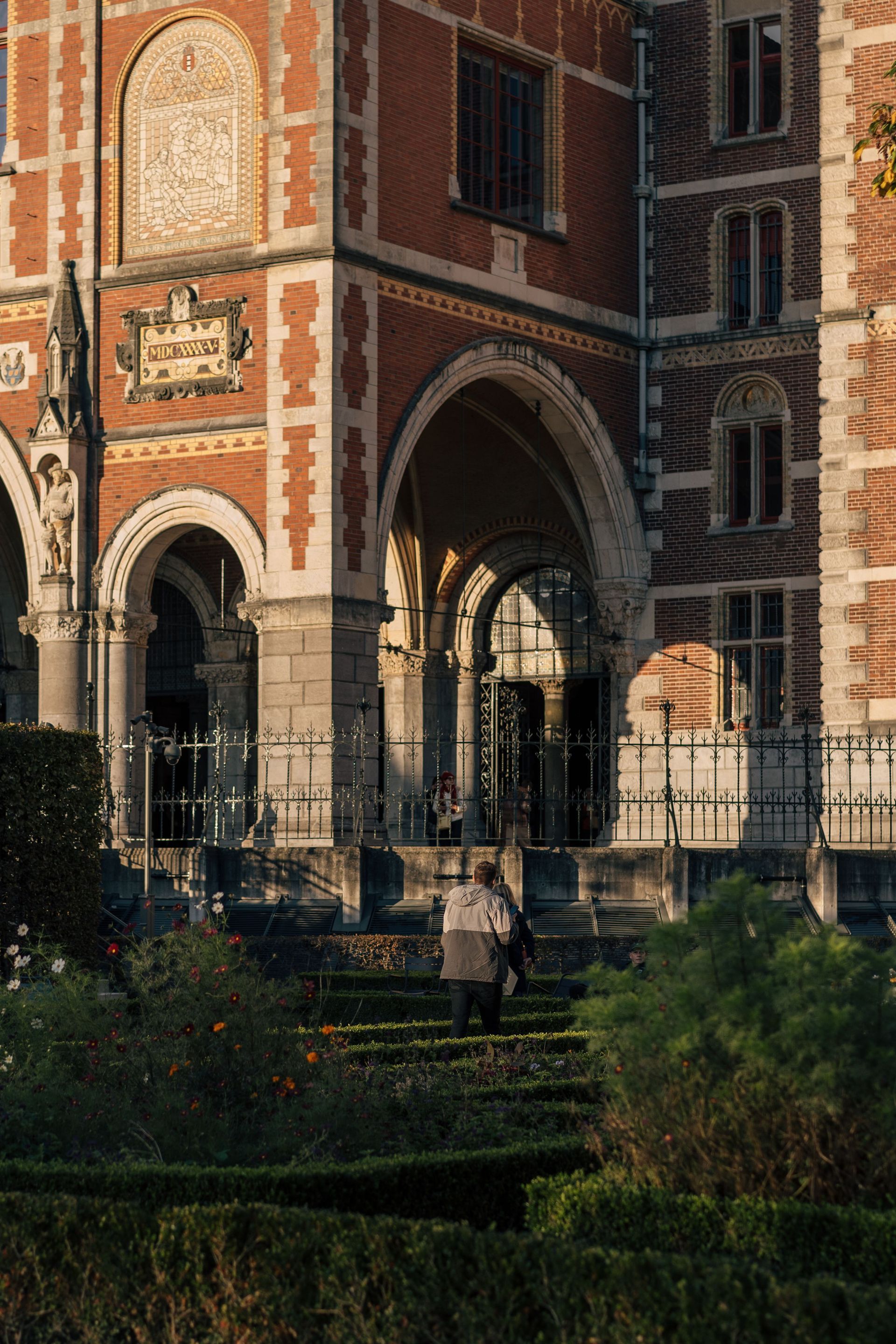 Ornate brick archway and iron gate in a garden, with a person walking below