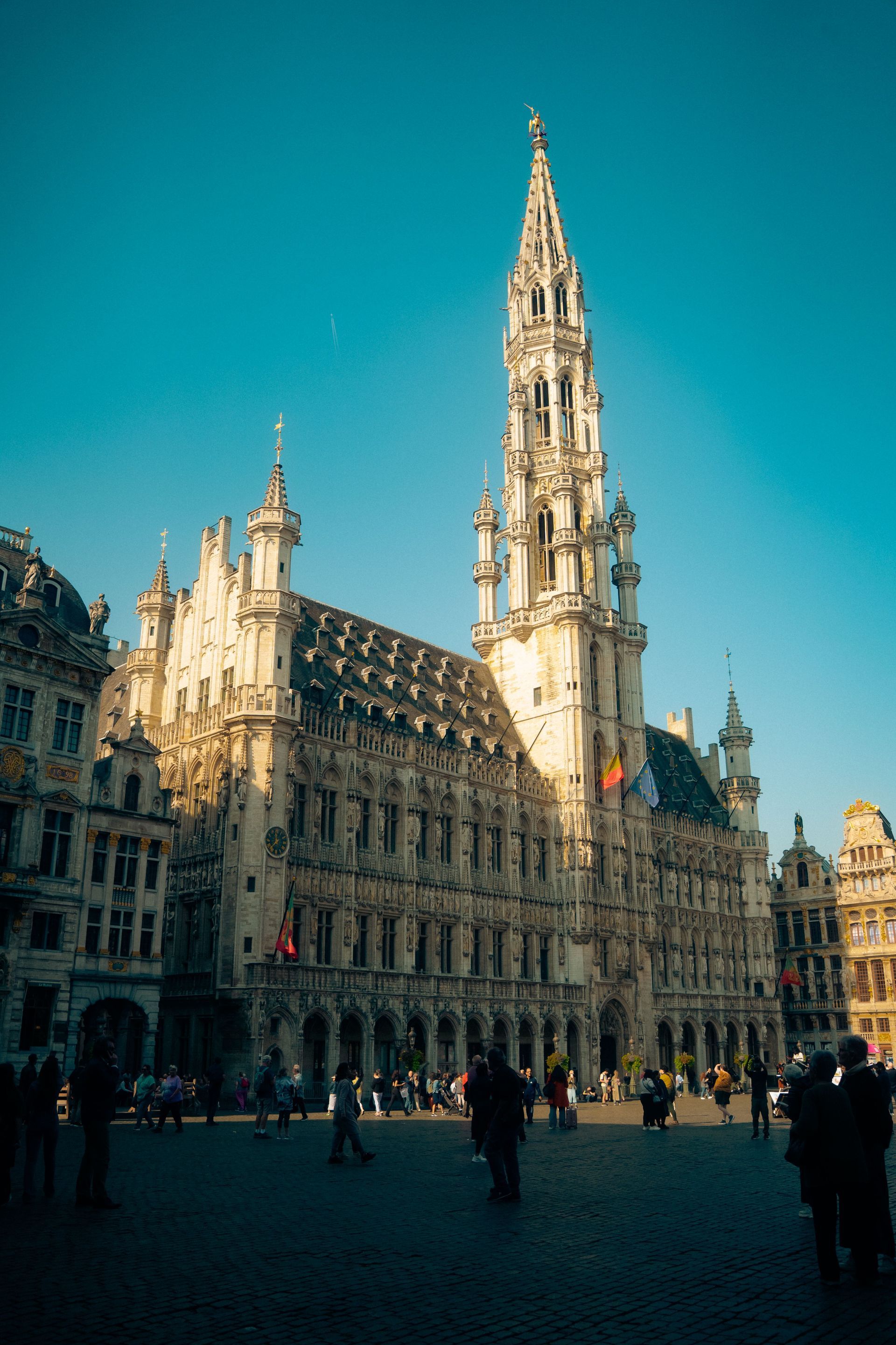 Historic Gothic city hall with a tall spire in a sunlit European square under a clear blue sky