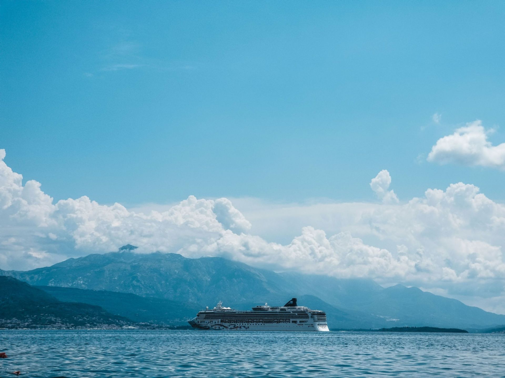 Cruise ship on calm blue water with mountains and clouds under a clear sky
