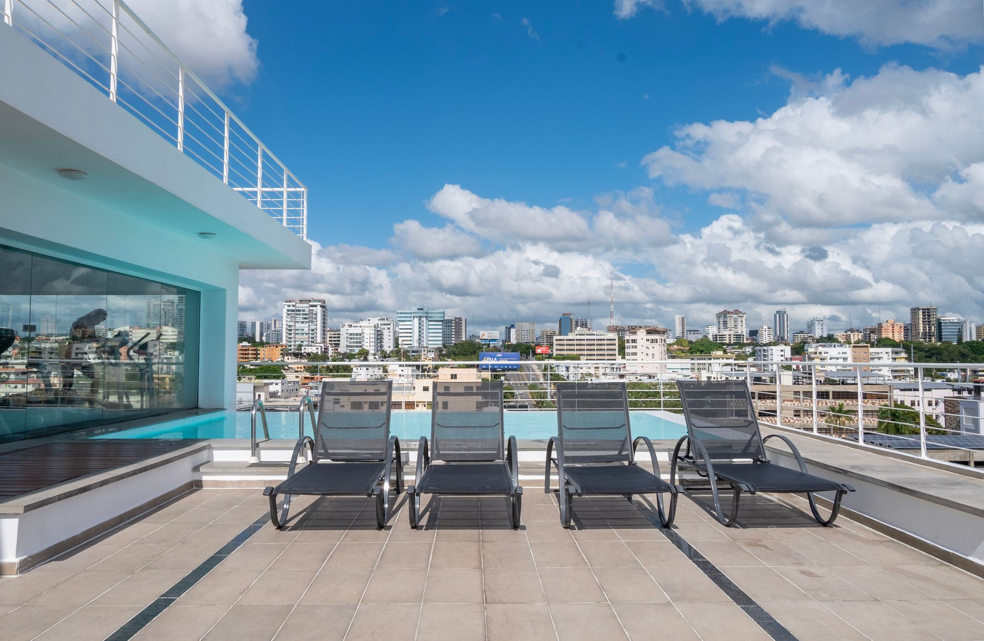 Terraza con piscina en la azotea y tumbonas con vistas al horizonte de la ciudad bajo un cielo azul.