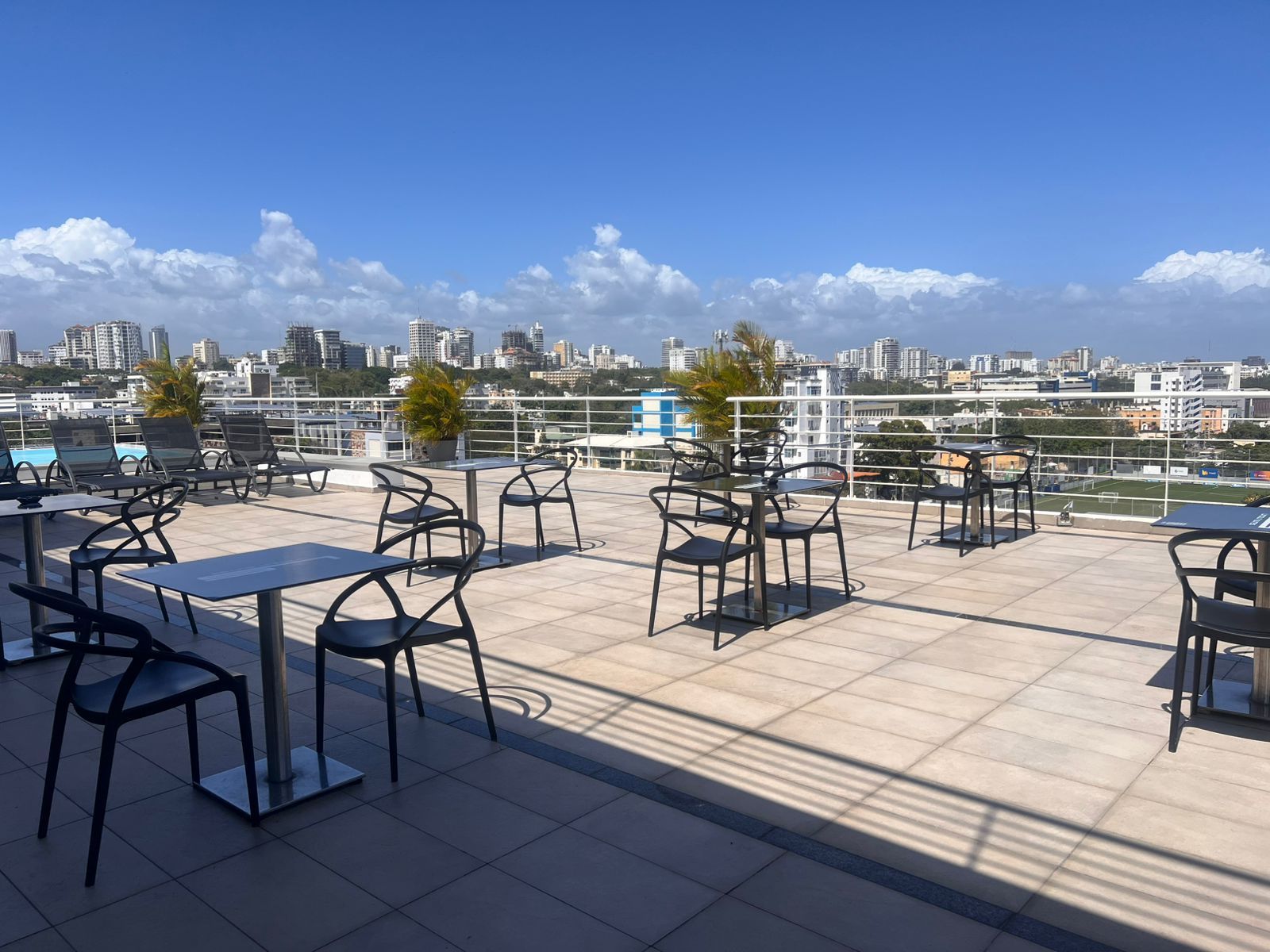 Terraza en la azotea con mesas y sillas vacías con vistas al horizonte de la ciudad bajo un cielo azul brillante.