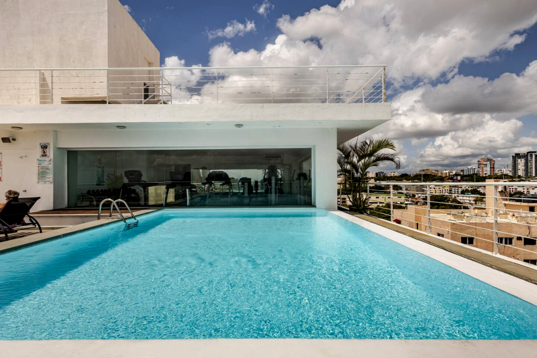 Piscina infinita en la azotea con agua turquesa junto a un edificio moderno bajo un cielo parcialmente nublado.