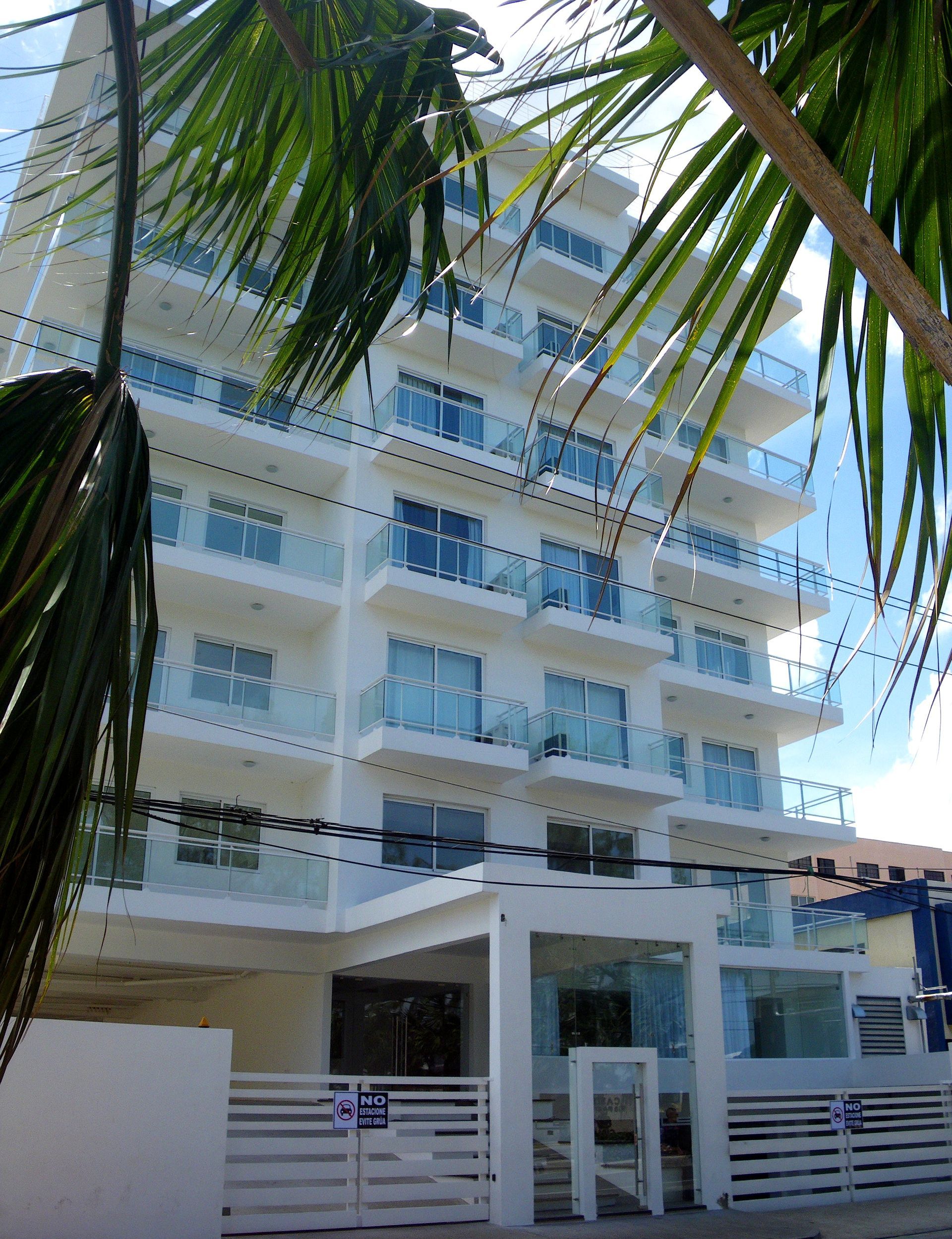 Edificio de apartamentos moderno de color blanco con balcones y entrada privada a pie de calle.