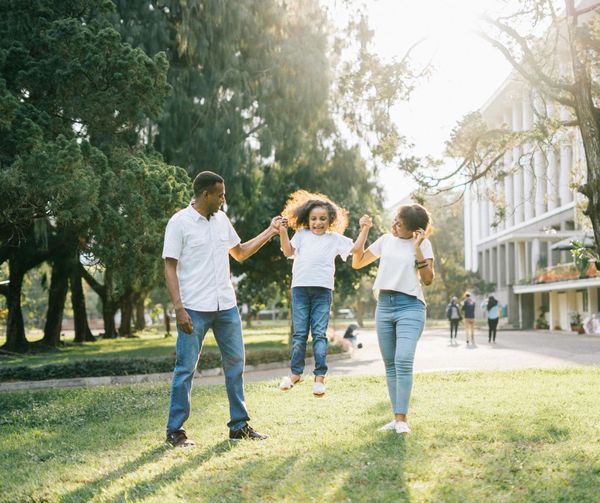Family playing in park; parents lifting child, sunny day.