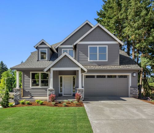 Gray suburban house with attached garage, front porch, and green lawn under a clear blue sky
