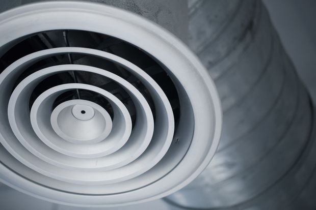 Close-up of a white circular ceiling vent with concentric rings on a gray ducted ceiling