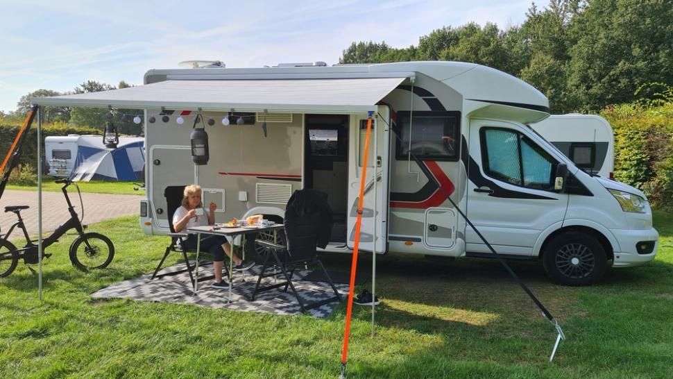 A Rv Is Parked In A Grassy Field With A Table And Chairs — Cairns Caravan Repairs In Edmonton, QLD