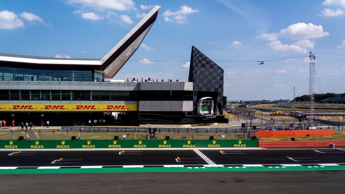 Formula 1 track with grandstand, pit lane, and a large angled roof at a racing circuit under a blue sky