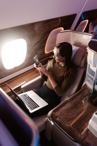 Woman using a laptop by an airplane window in a business-class seat