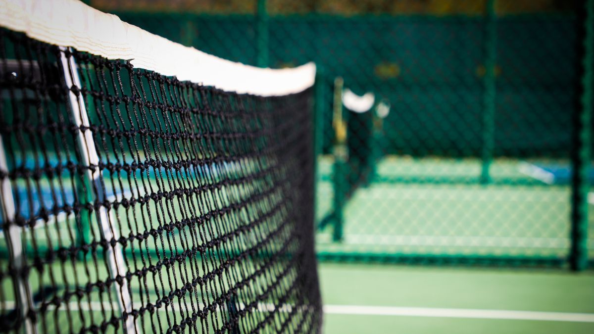 Tennis net in the foreground on an outdoor court with a green background