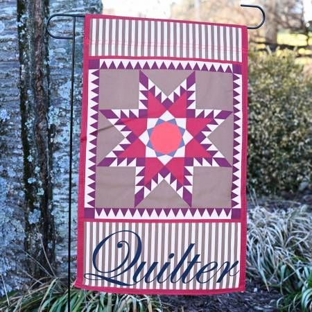 Quilted hanging with red, pink, and beige starburst pattern on a tree trunk outdoors