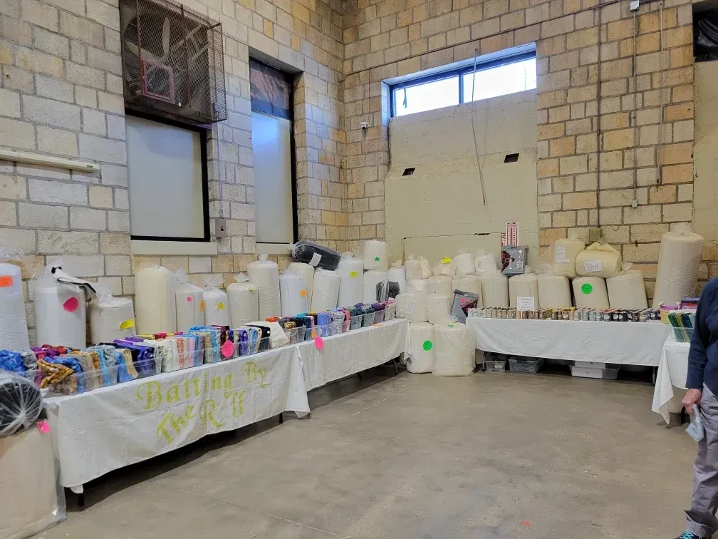 Table of assorted colorful household items in a stone-walled room with a child at right edge