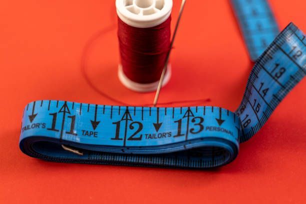 Blue measuring tape wrapped around a red spool on a bright red background