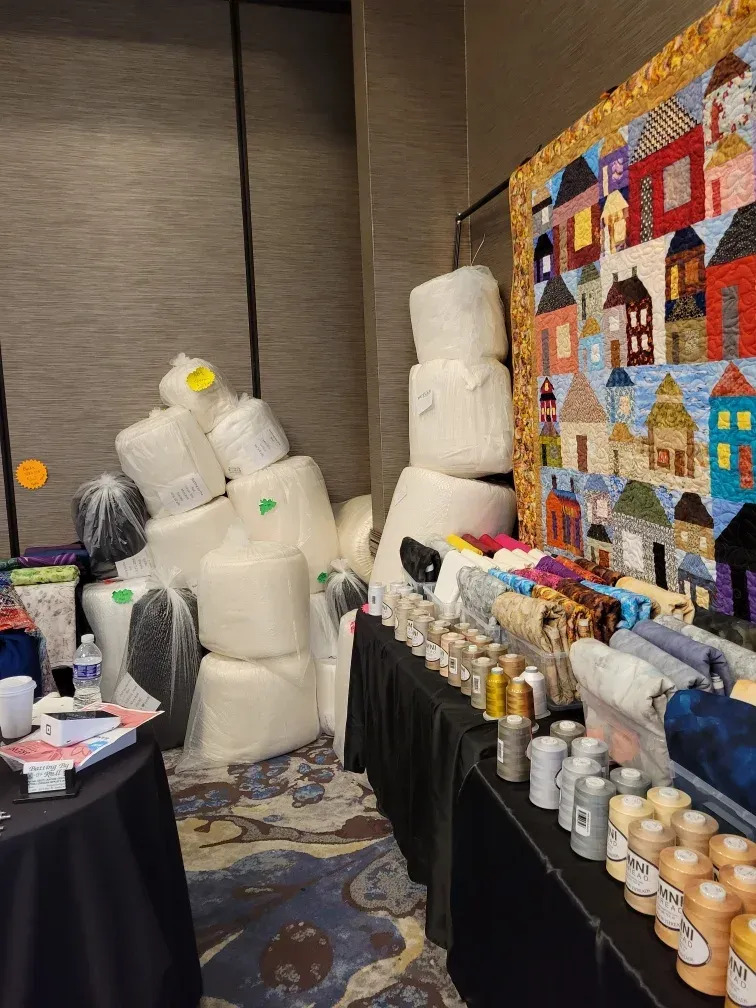 Stacked foam bear sculptures beside a quilt display and jars on vendor tables in a conference room