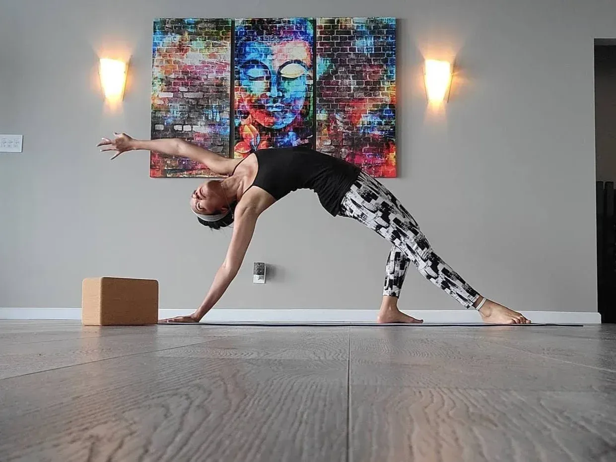 Person doing a yoga bridge pose in a studio, reaching back toward a wooden block.