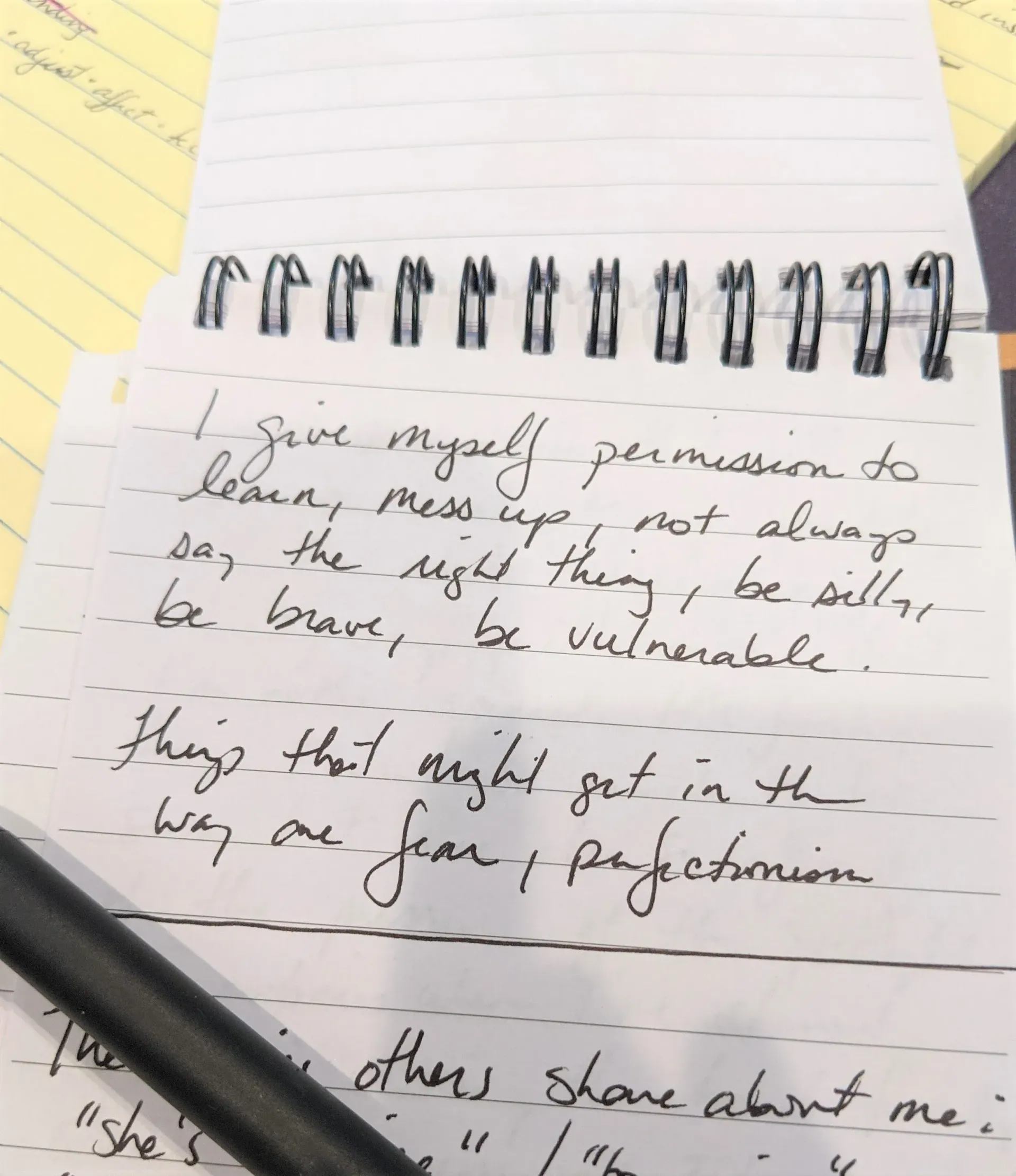 Notebook page with handwritten notes, black pen, and a pencil across the bottom on a yellow surface