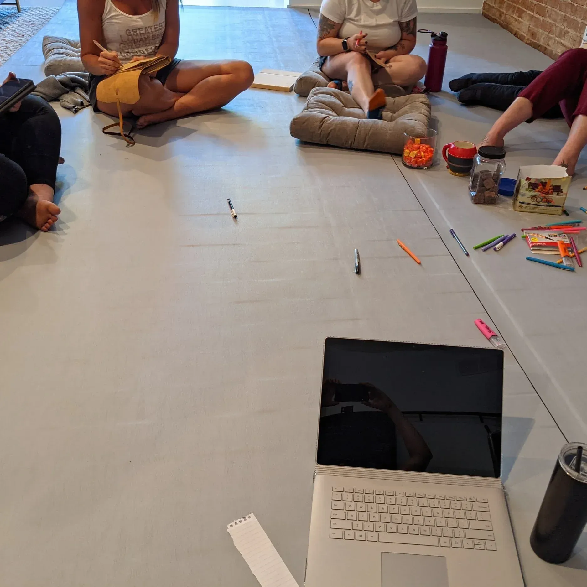 People sitting on a floor around art supplies and a laptop in a bright room