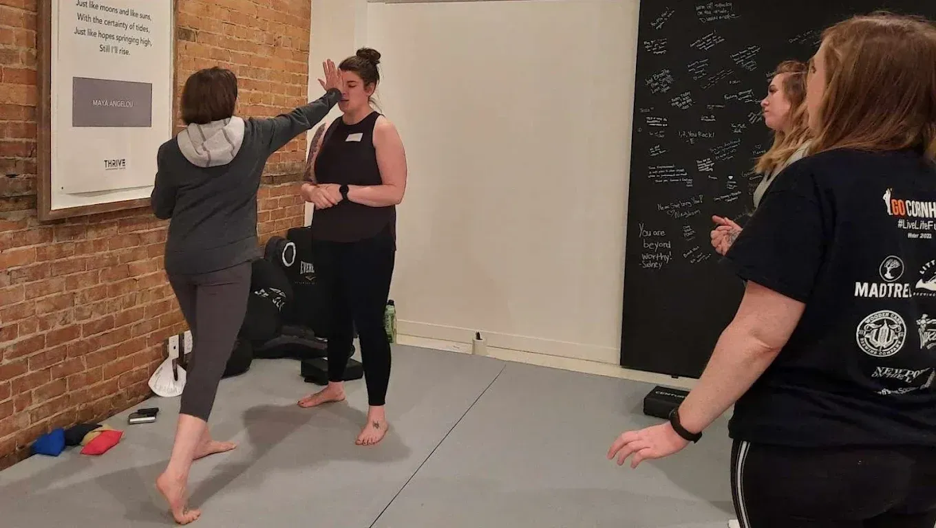 Two people sparring in a martial arts studio, one holding a raised kick while the other blocks.