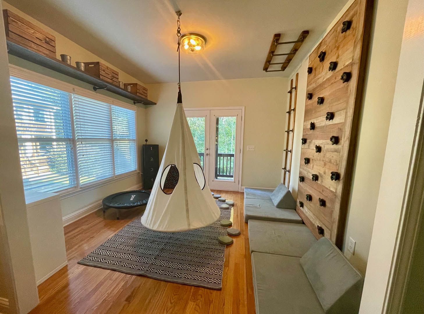 A room with a teepee hanging from the ceiling and a climbing wall.