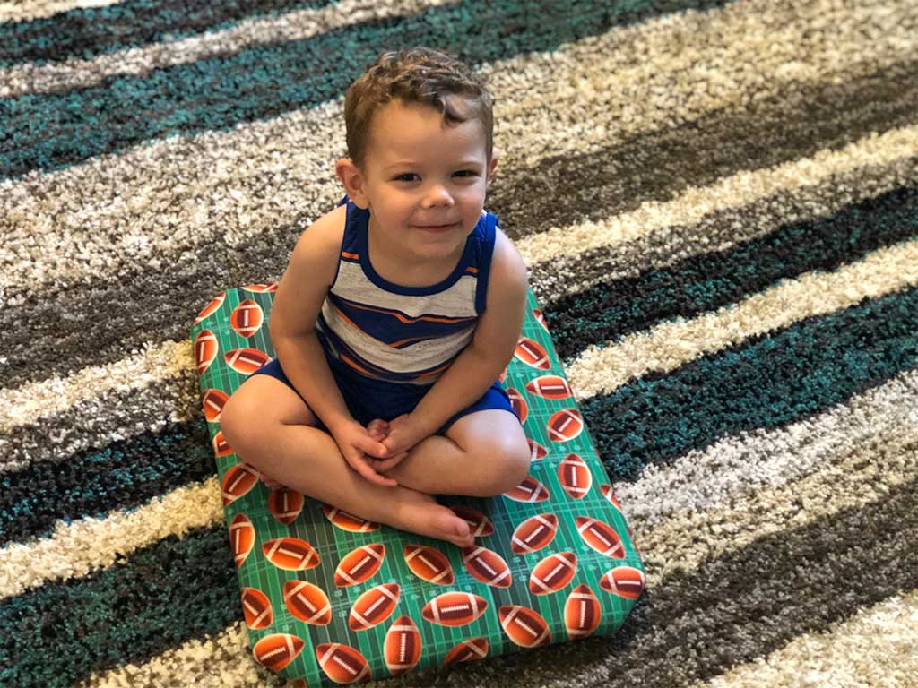 A young boy is sitting on a pillow on a rug.