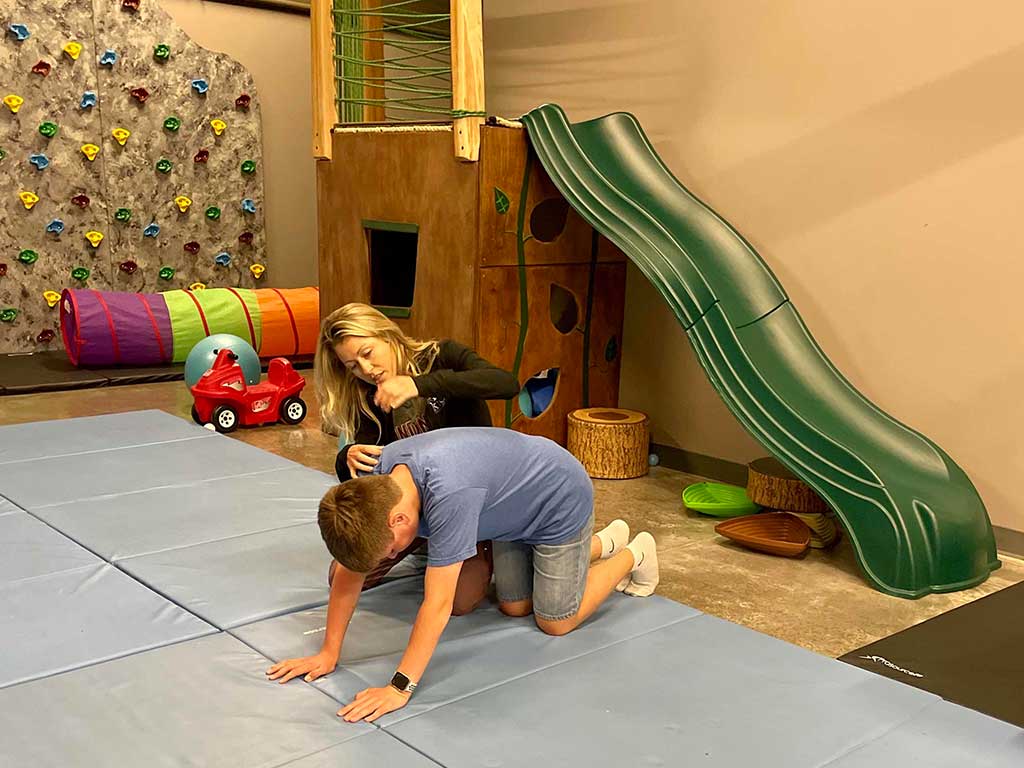 A woman is petting a boy on the floor in a playground.