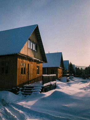 Snow-covered wooden cabins at dusk, with blue roofs and soft sunset light