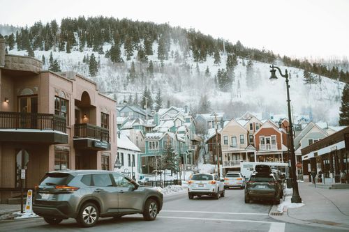 Snowy mountain town street with cars, storefronts, and misty hills in the background