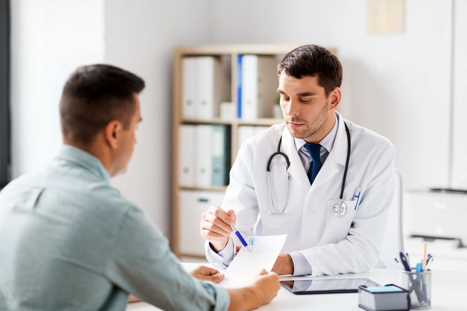 Doctor in white coat reviews paperwork with male patient in an office.