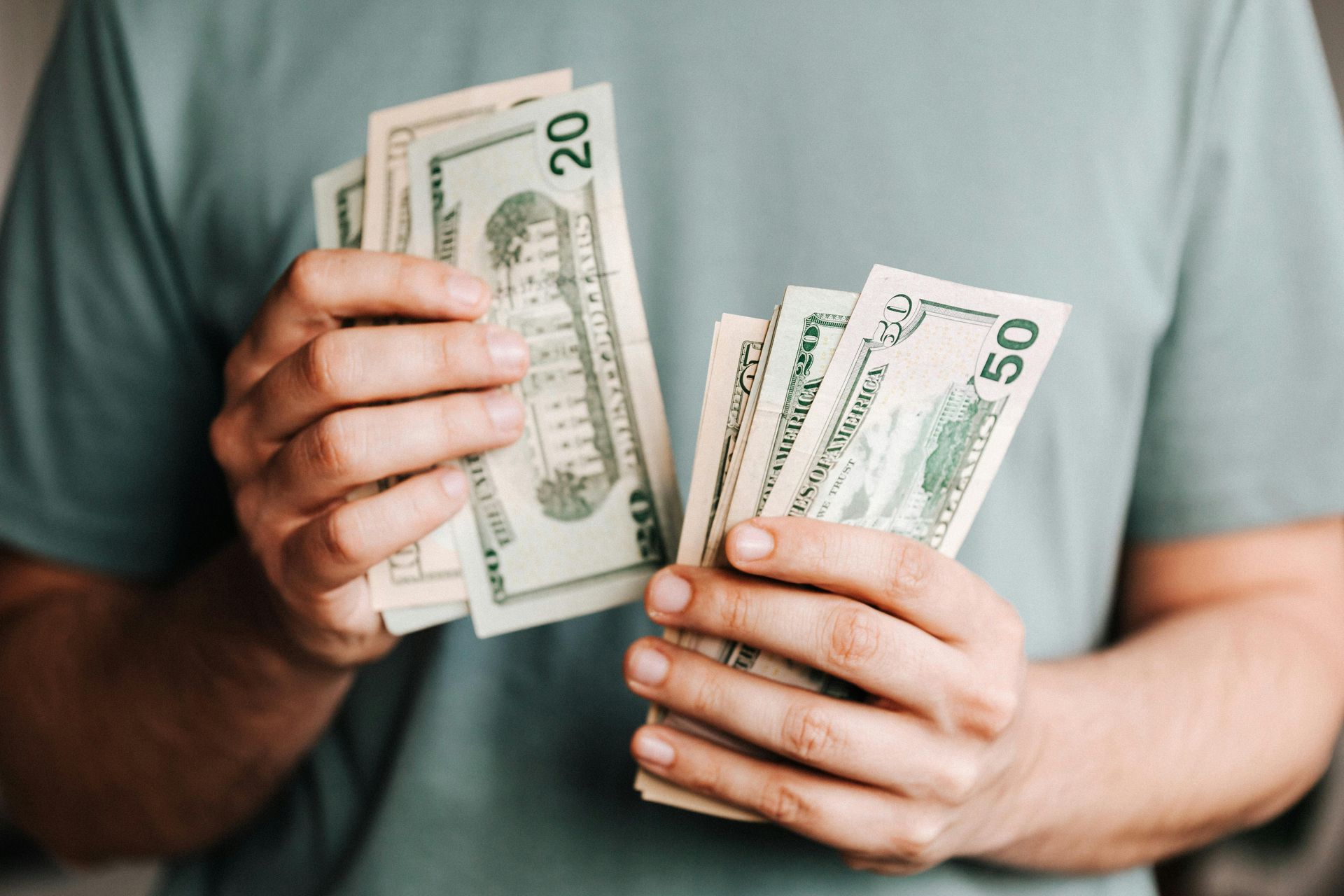 Person holding a stack of twenty and fifty dollar bills.