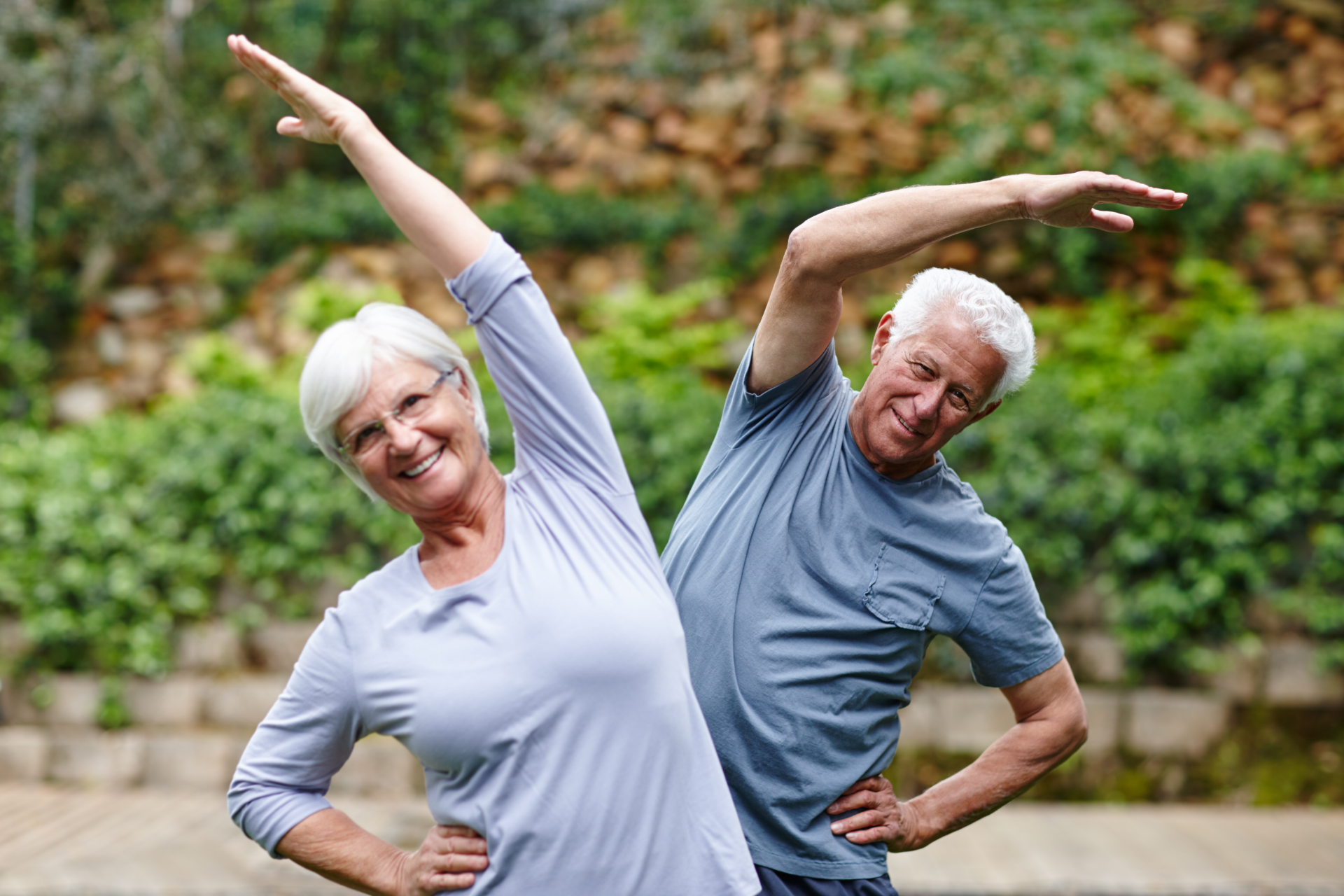 Senior couple stretching outdoors, arms raised, smiling.
