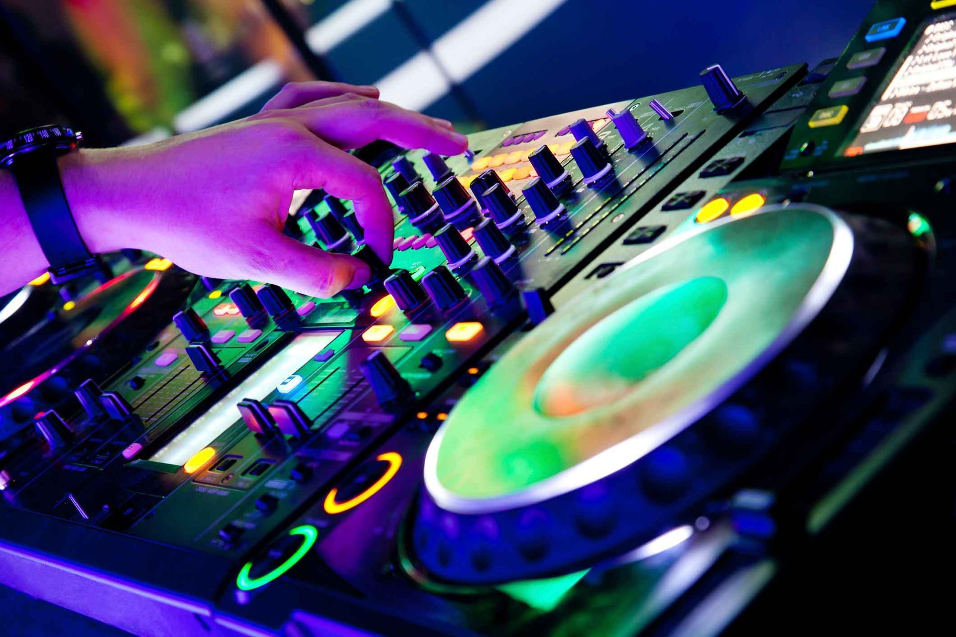 A dj is playing music on a mixer in a dark room.
