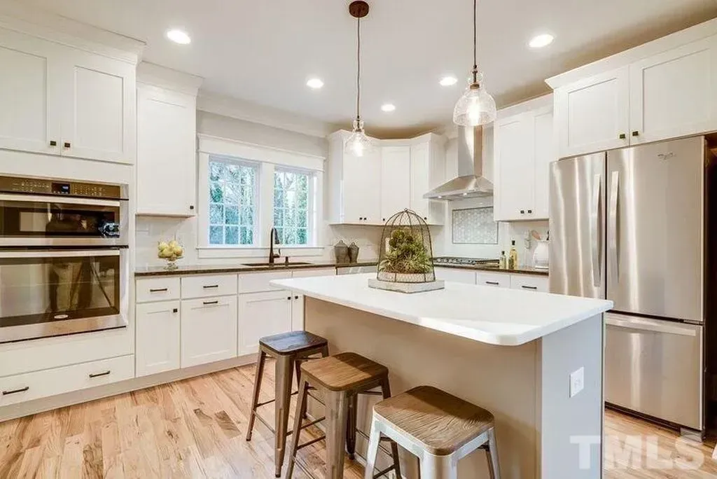 Bright white modern kitchen with island, stainless steel fridge, and wood stools
